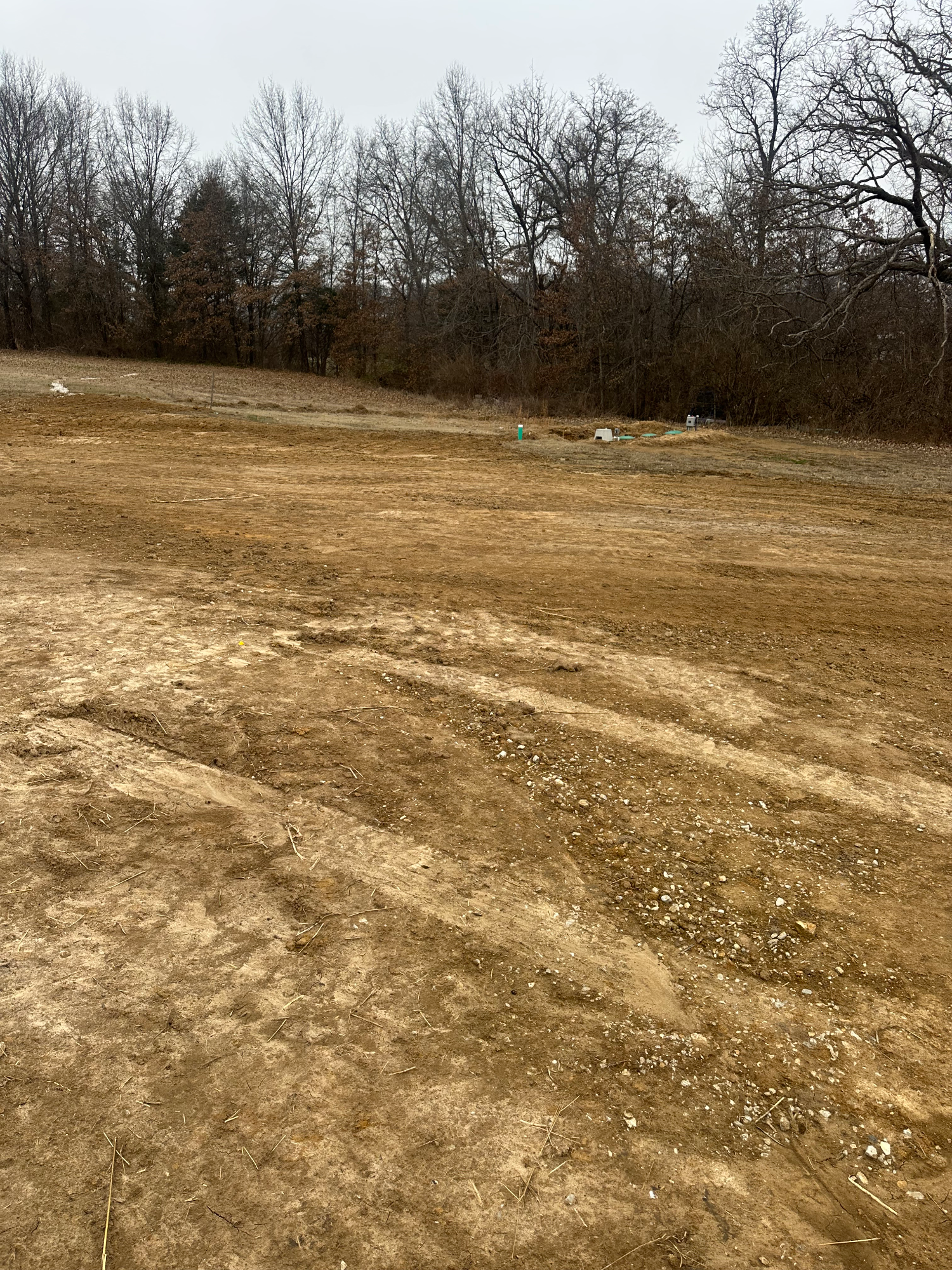 Rough ungraded yard around a new construction home in Moscow Mills with uneven soil and no drainage established